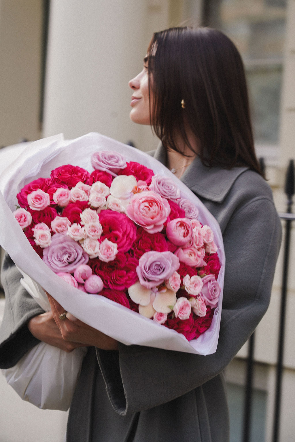 Woman holding a bouquet of pink and white roses outdoors.